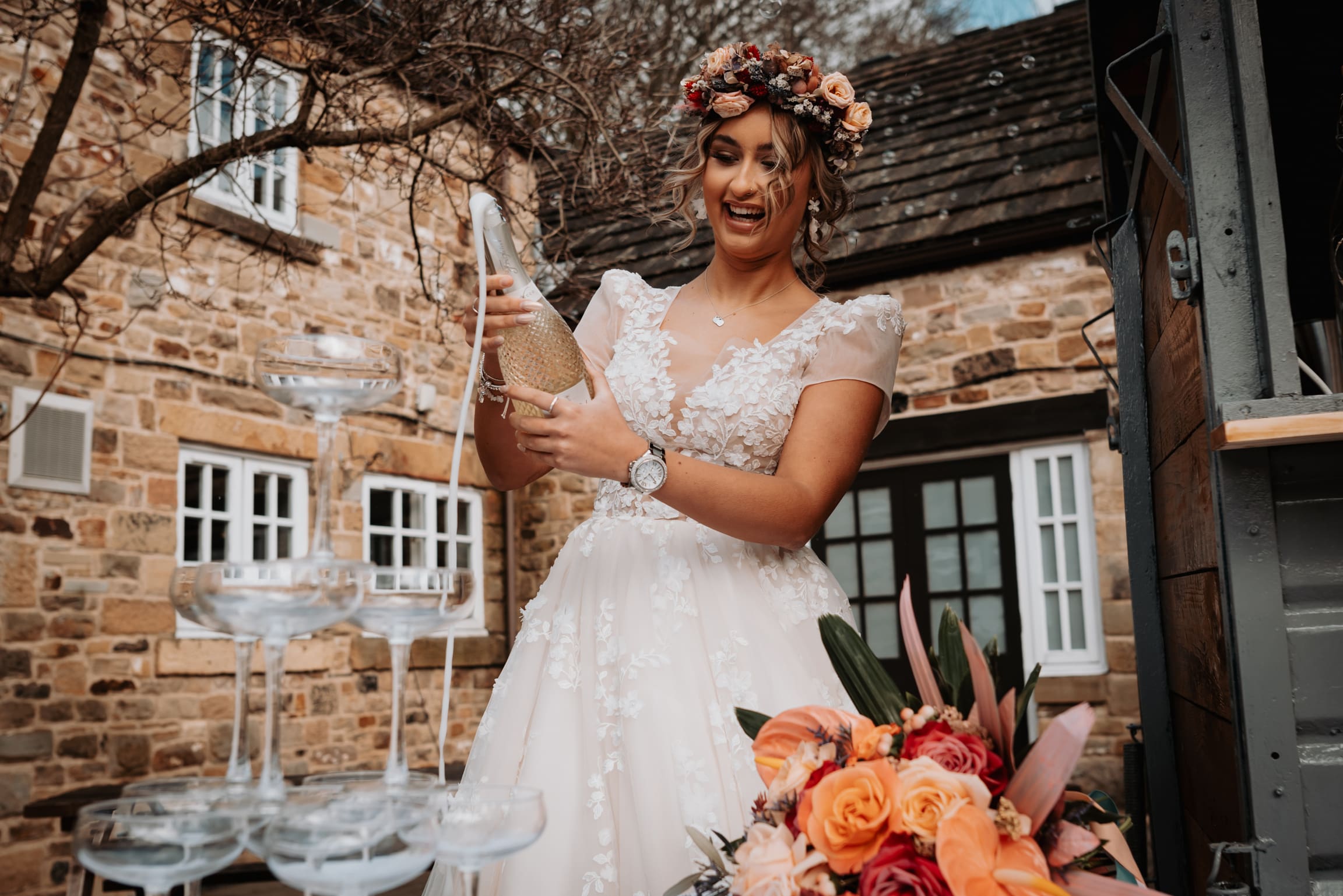A bride pouring a bottle of Prosecco over a champagne tower.