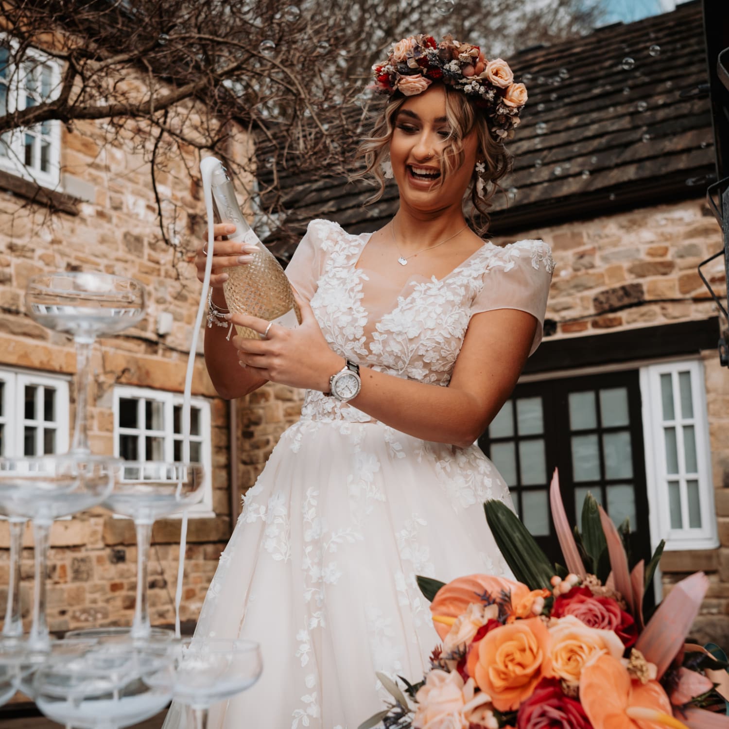 A bride pouring a bottle of Prosecco over a champagne tower.